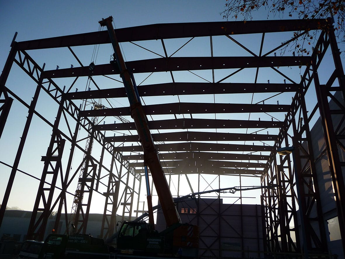 Hallenrichtmontage bei Dämmerung – ein Stahltragwerk von Stahlbau Döring mit Mobilkran, die Sonne scheint durch die Binder.