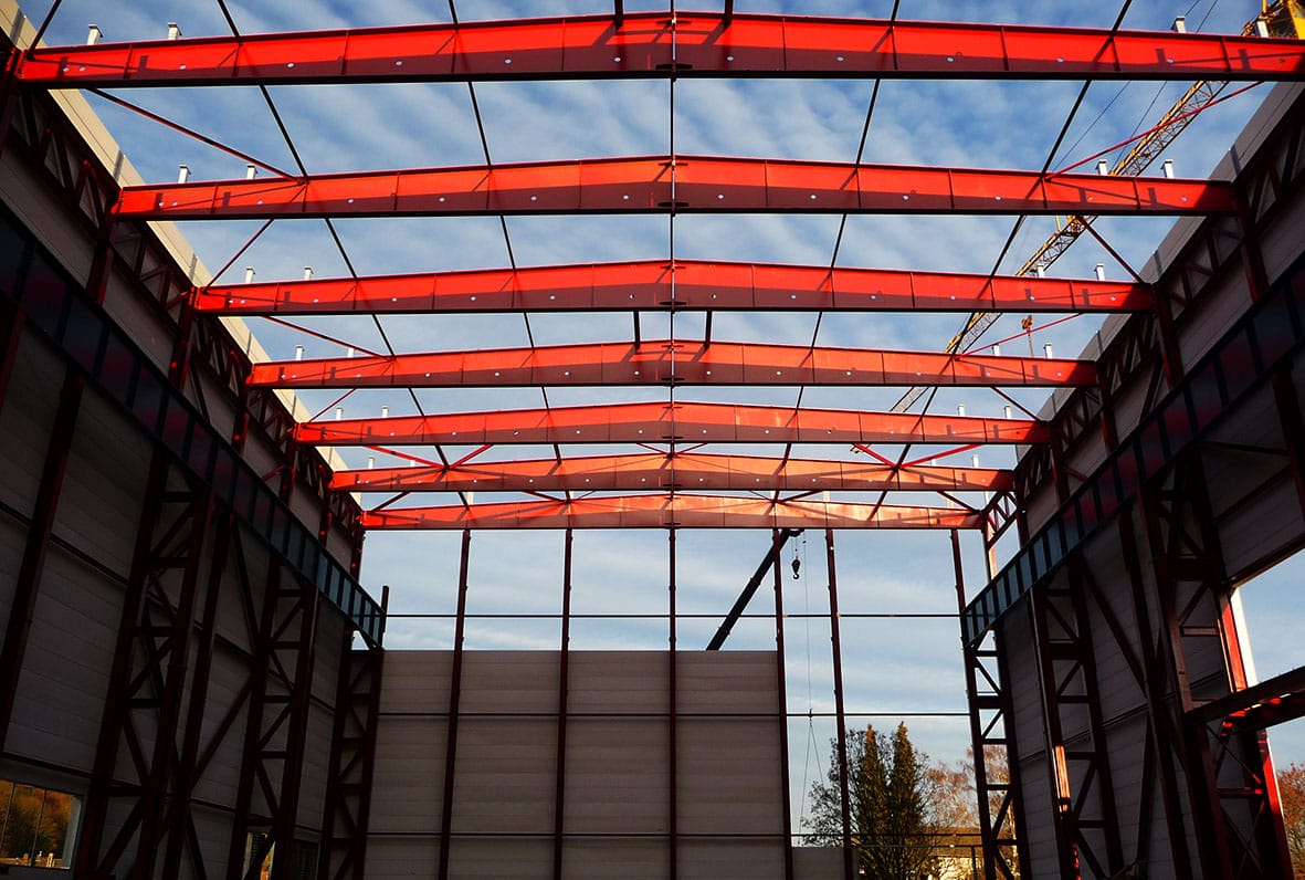 Rot grundiertes Stahltragwerk einer Halle bei Sonnenuntergang, von innen fotografiert.